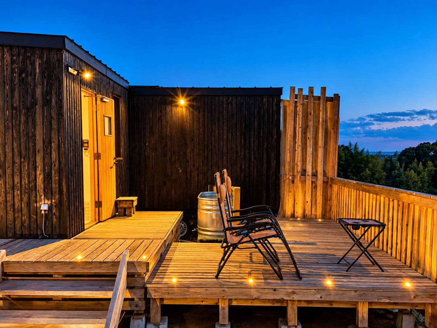 A wooden deck with a metal barrel, chairs, and a small table.