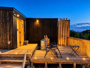 Une terrasse en bois avec un tonneau en métal, des chaises et une petite table.