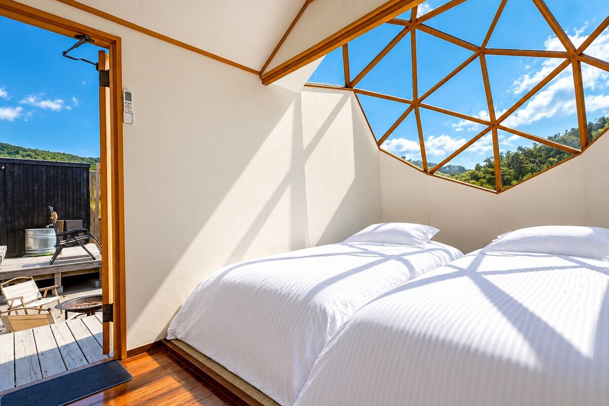 Een slaapkamer met een houten balken plafond, een bed en uitzicht op de omgeving.