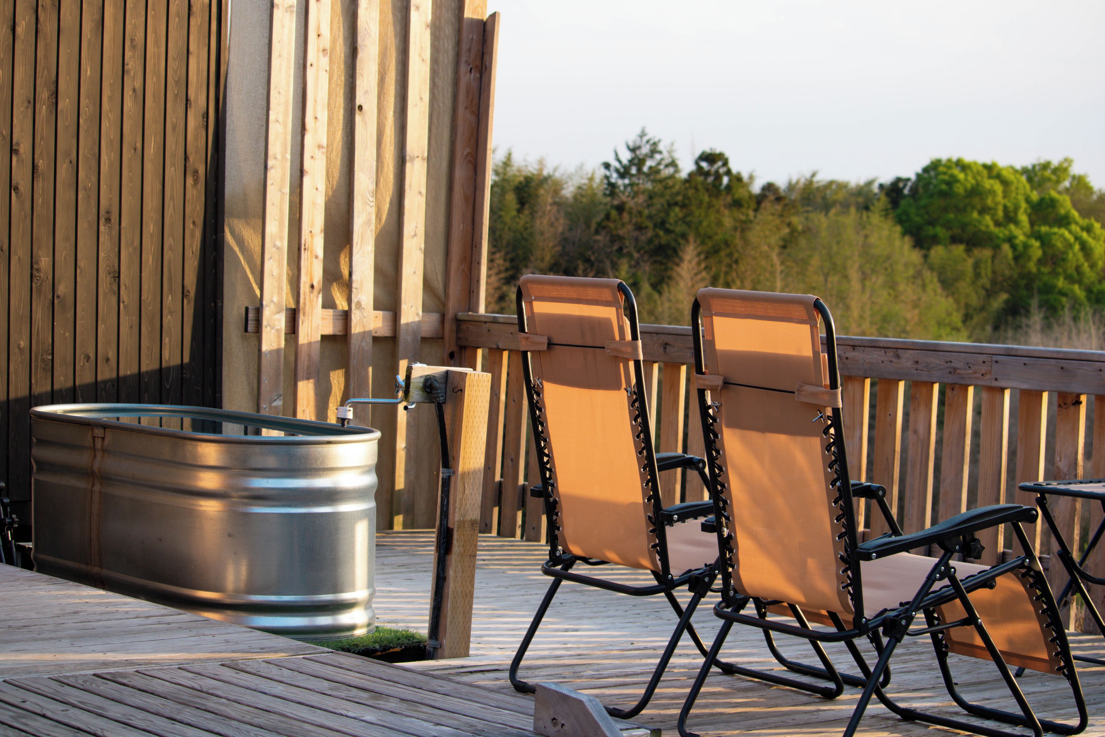 A wooden deck with two foldable chairs and a metal trash can.