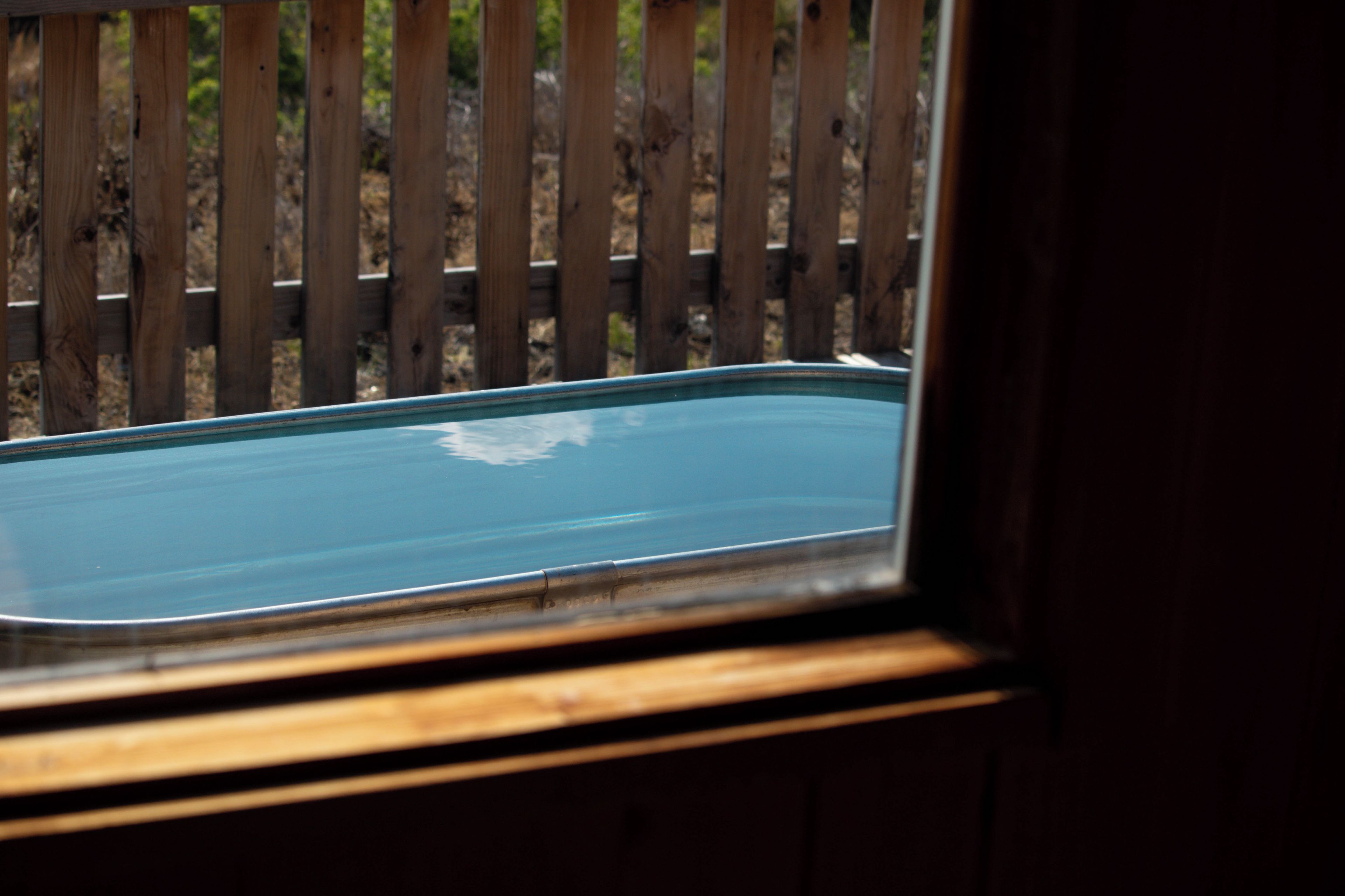 A view through a window with a wooden frame, looking out onto a wooden fence and a blue surface, possibly a pool or water feature.