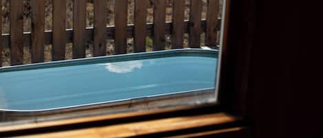 Vista a través de una ventana con marco de madera, que da a una cerca de madera y una superficie azul, posiblemente una piscina o una fuente de agua.