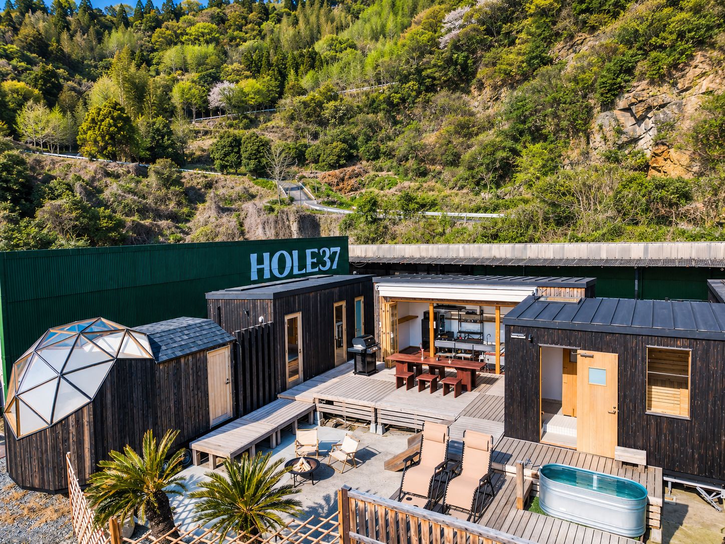 A modern outdoor lounge area with a pool, wooden deck, and a sign reading 'HOLE37'.