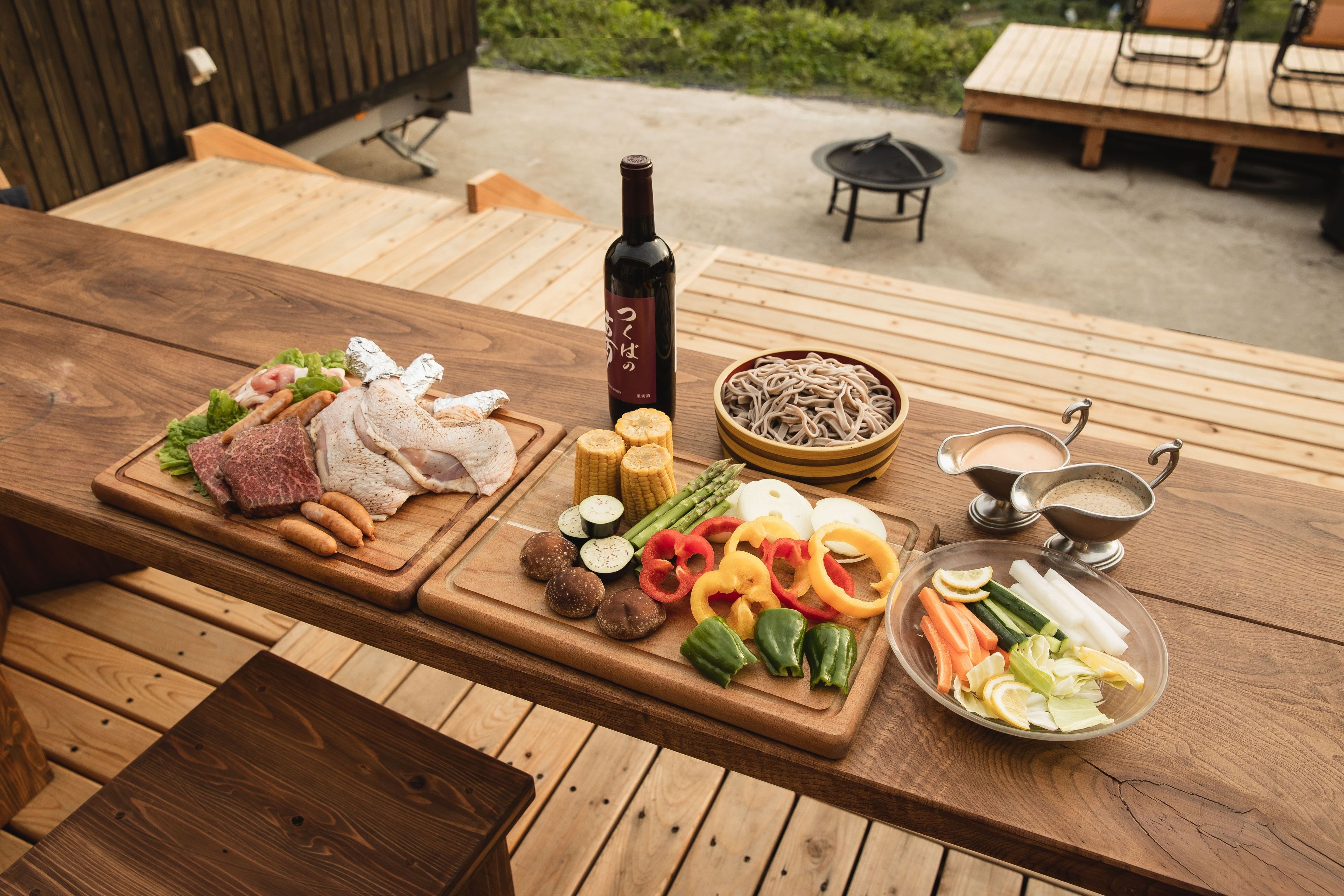 A wooden table with a variety of food items including meats, vegetables, and a bottle of wine.