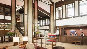 A spacious lobby with a leather sofa, a wooden reception desk, and a staircase. - HOLE37 (Tsukuba)