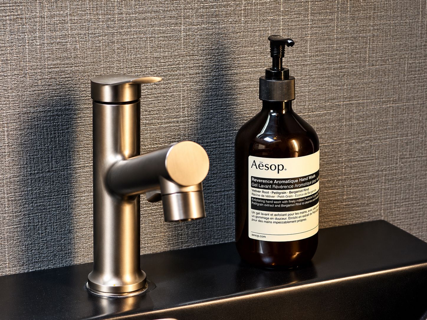 A bathroom with a modern faucet and a bottle of hand wash soap.