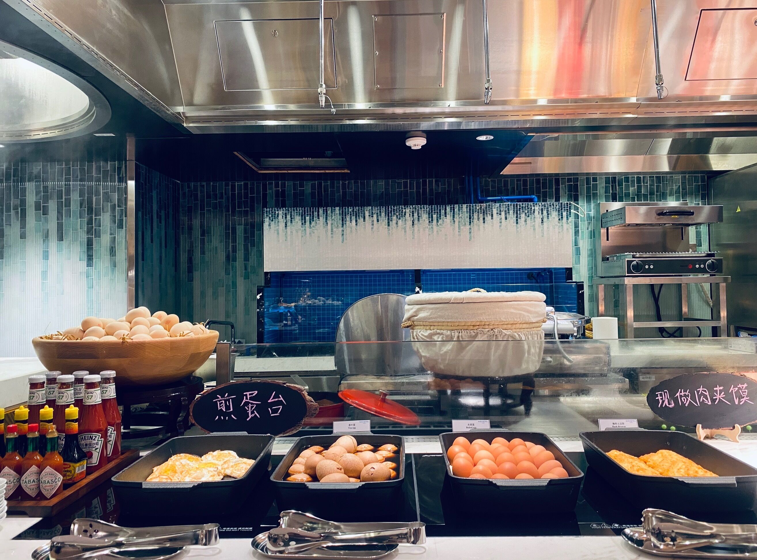 A buffet area with various food items, condiments, and a large stainless steel appliance in the background.