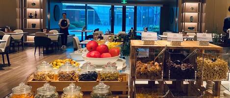 A buffet area with various food items and a seating area with tables and chairs.