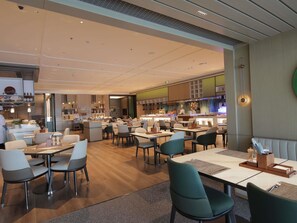 Ein modernes Restaurant mit mehreren Essbereichen, einer Bar und einer sichtbaren Küche.