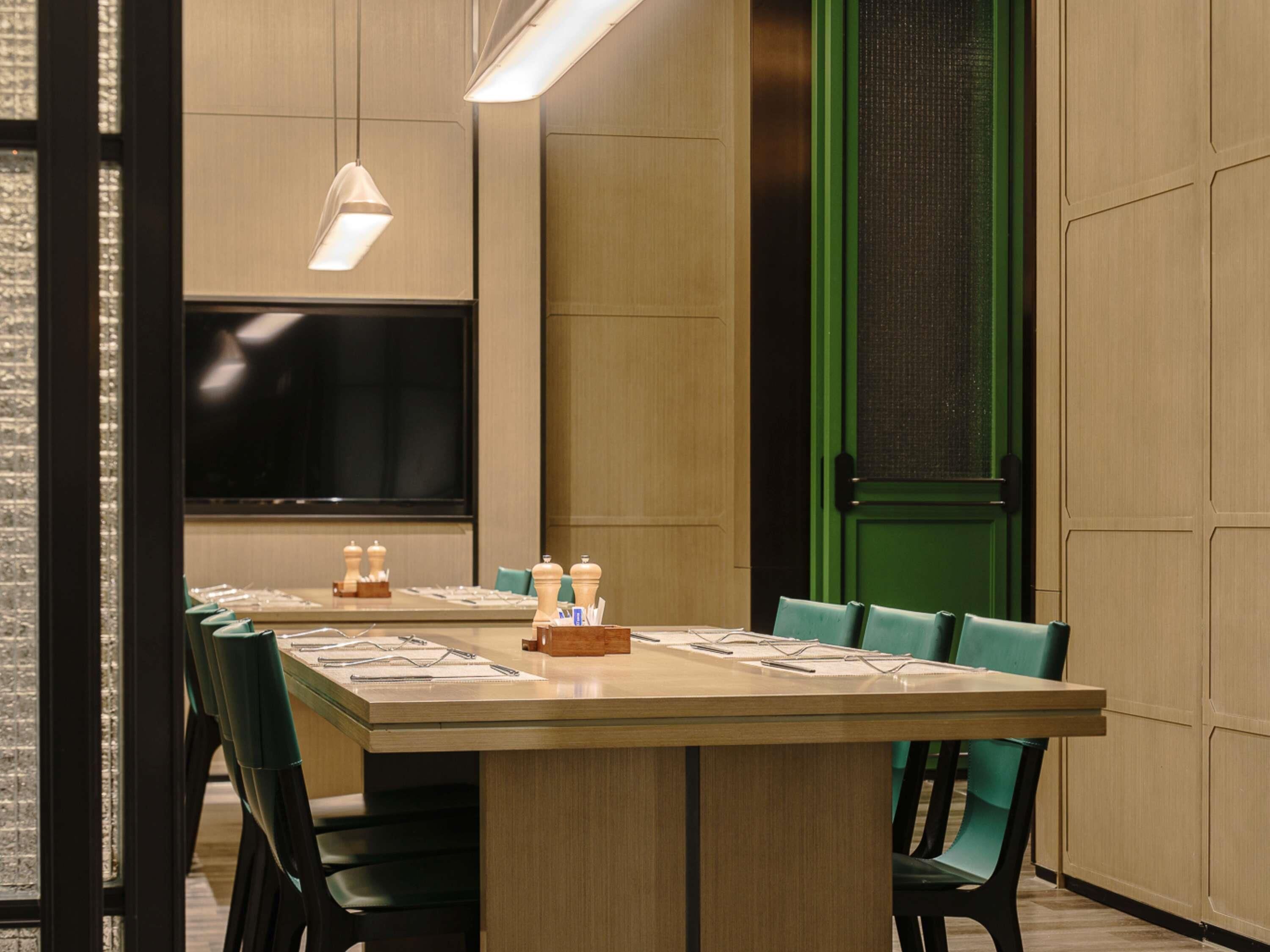 A conference room with a long table, green chairs, a large screen, and a green door.