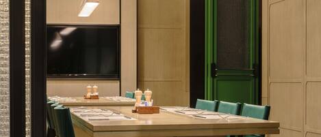 A conference room with a long table, green chairs, a large screen, and a green door.