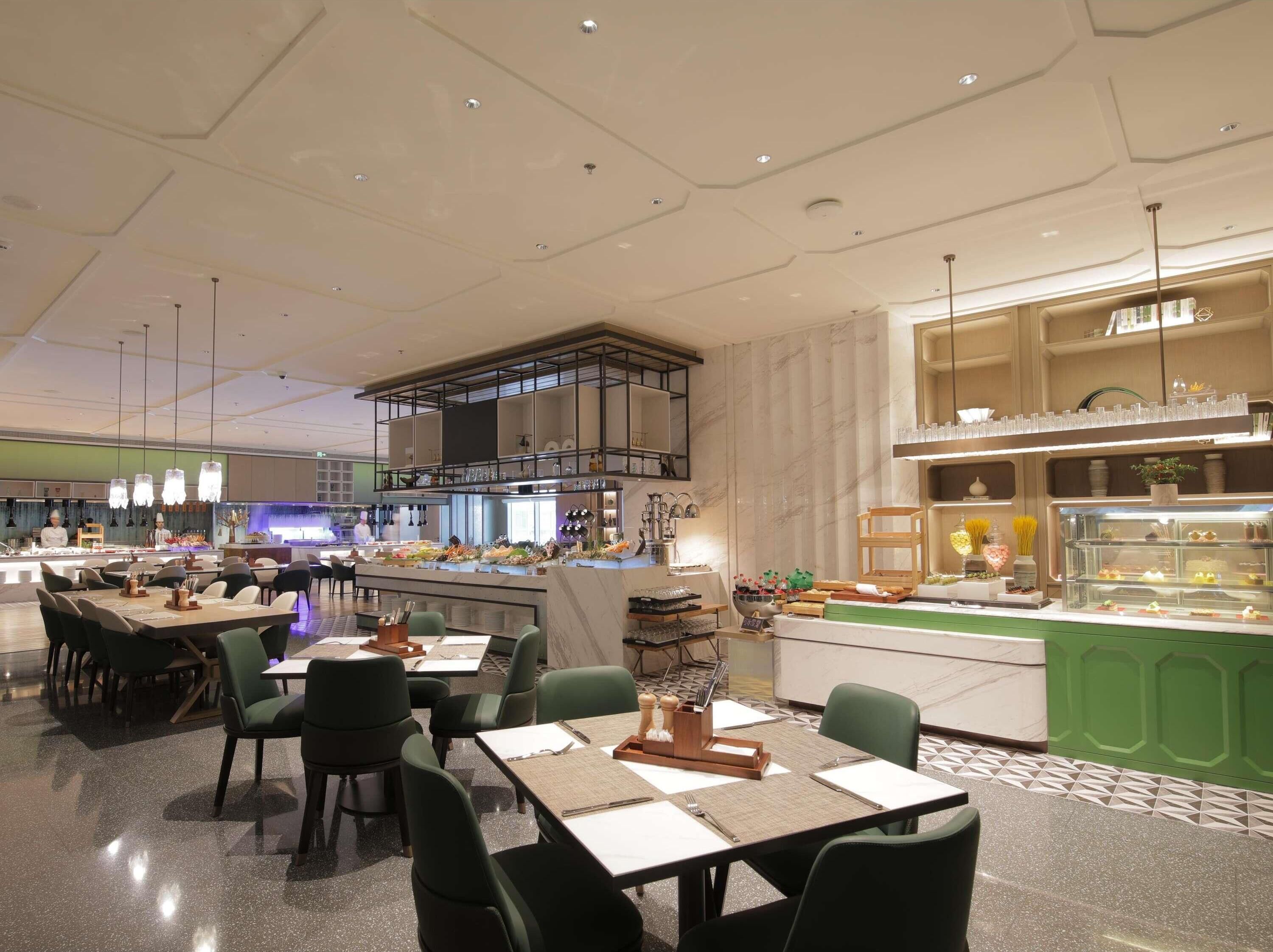 A modern restaurant with a bar area, multiple dining tables, and a buffet counter.