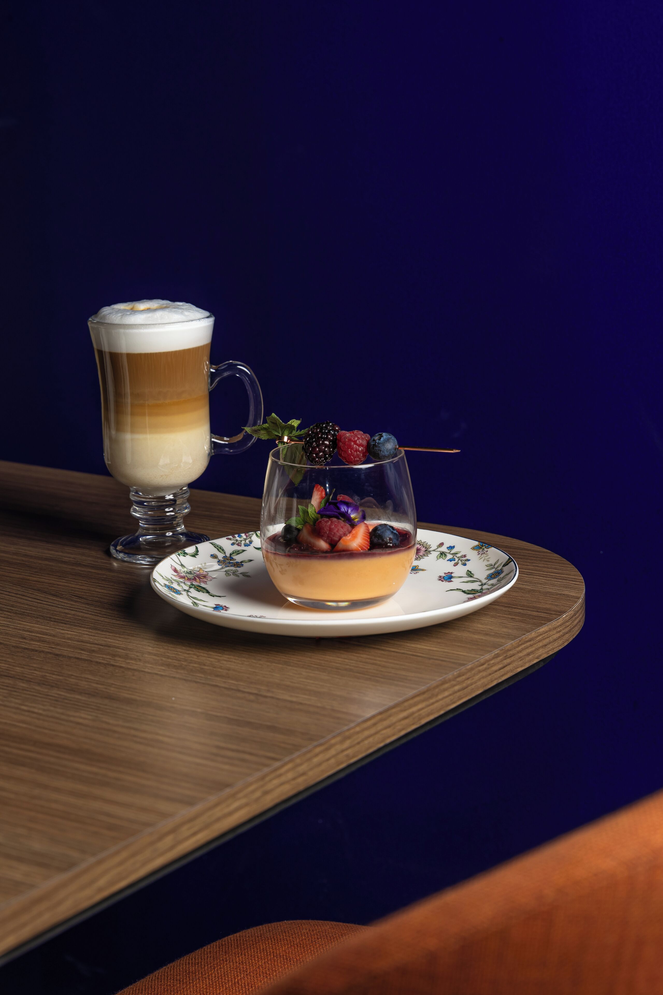 Un postre con bayas y un vaso de bebida en capas sobre un plato floral.
