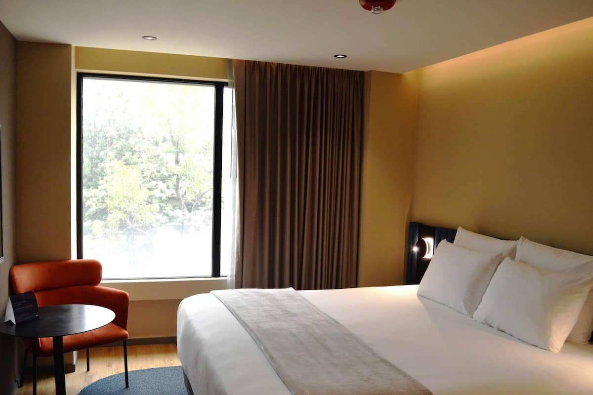 Una habitación de hotel con cama, una silla, una mesa y una ventana con cortinas.