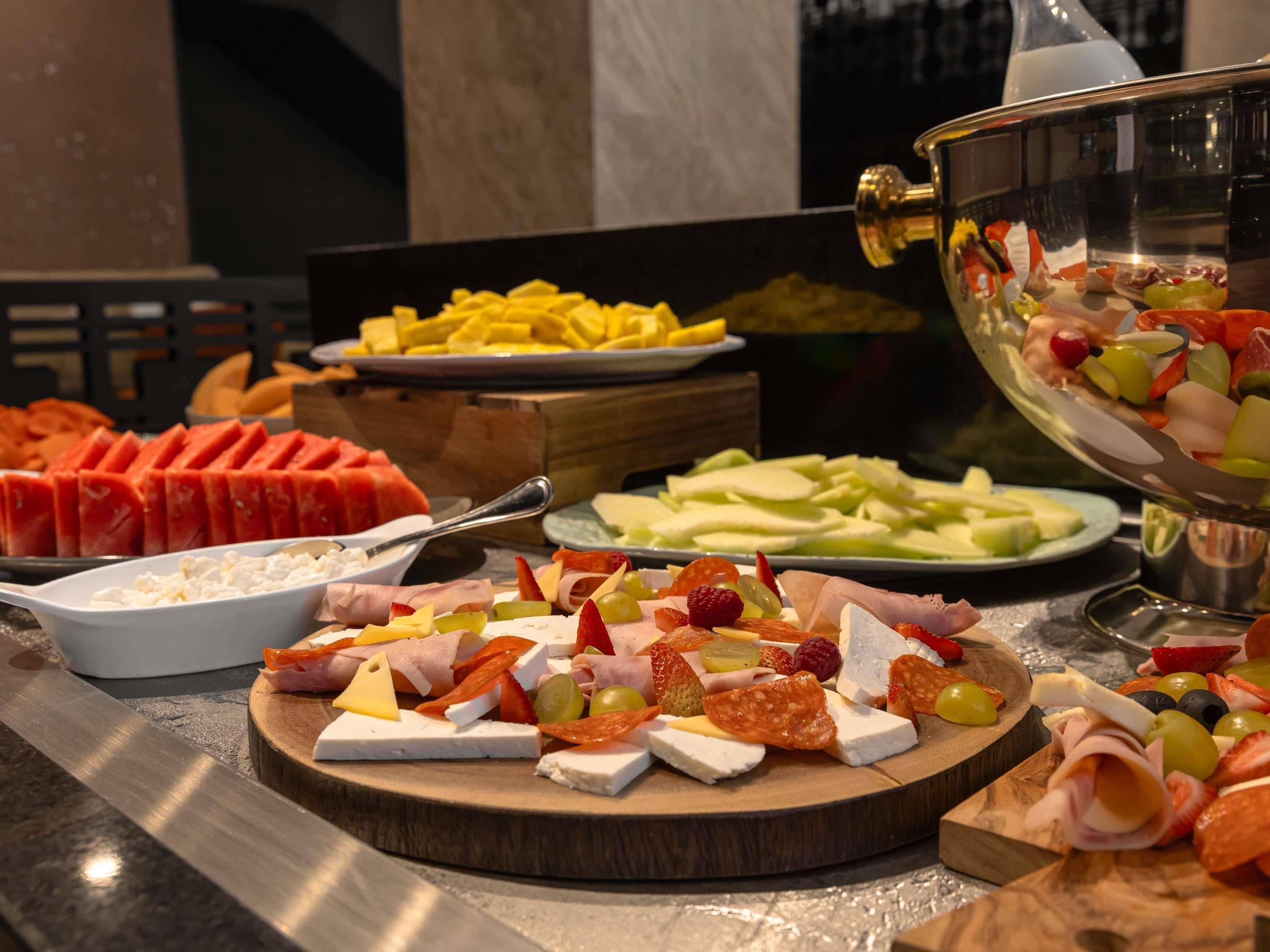 A buffet with various cheeses, meats, fruits, and vegetables.