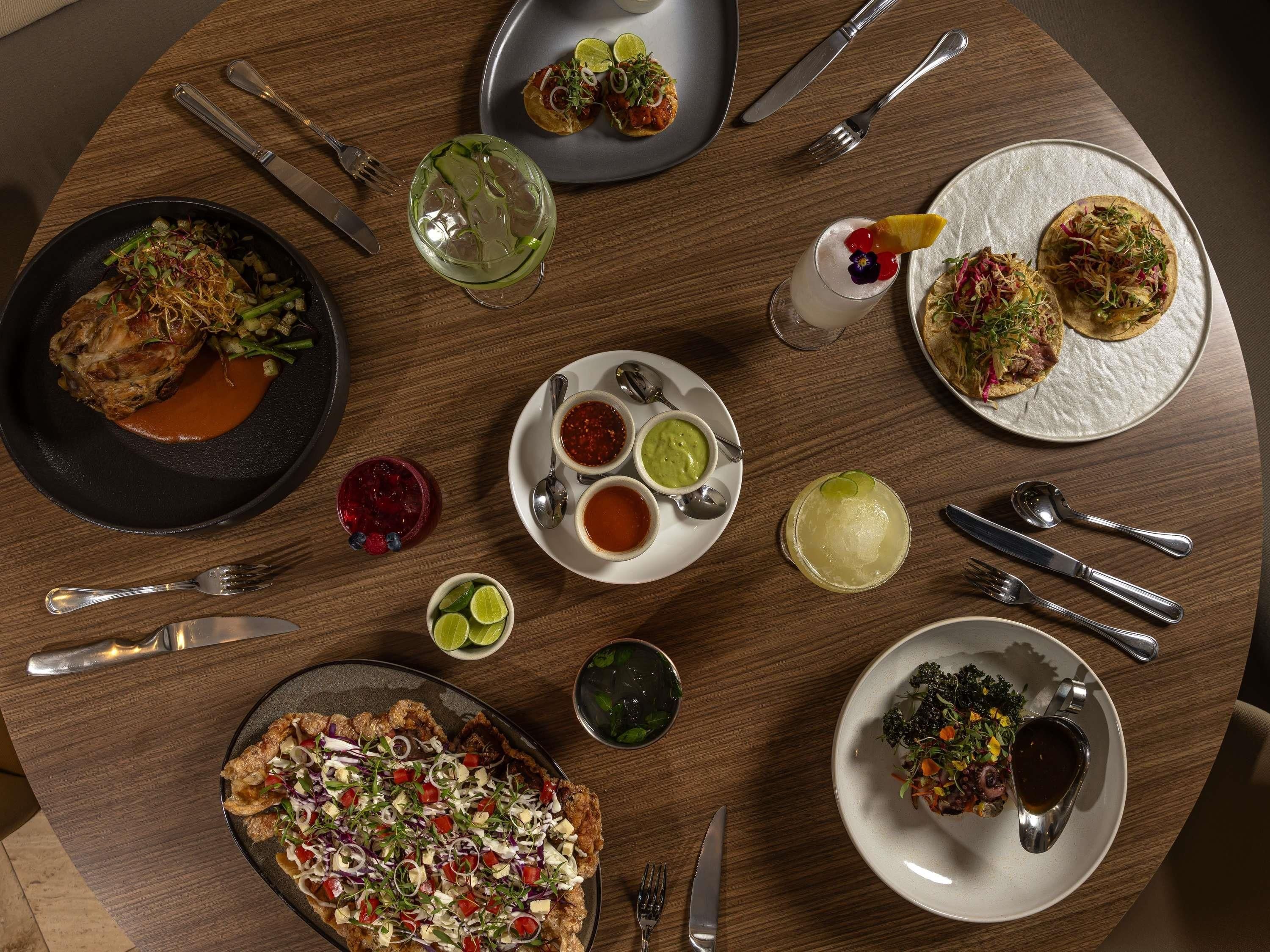Una mesa redonda con varios platos, como tacos, ensalada y un plato de pescado, además de bebidas y salsas.