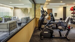 Ein modernes Fitnessstudio mit Trainingsgeräten, einer Sitzecke mit Stühlen und einem Tisch sowie einem Blick durch eine Glaswand.