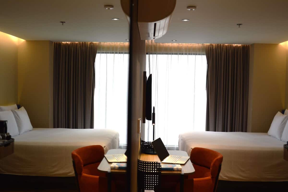 A hotel room with two beds, a desk with a laptop, and a chair.