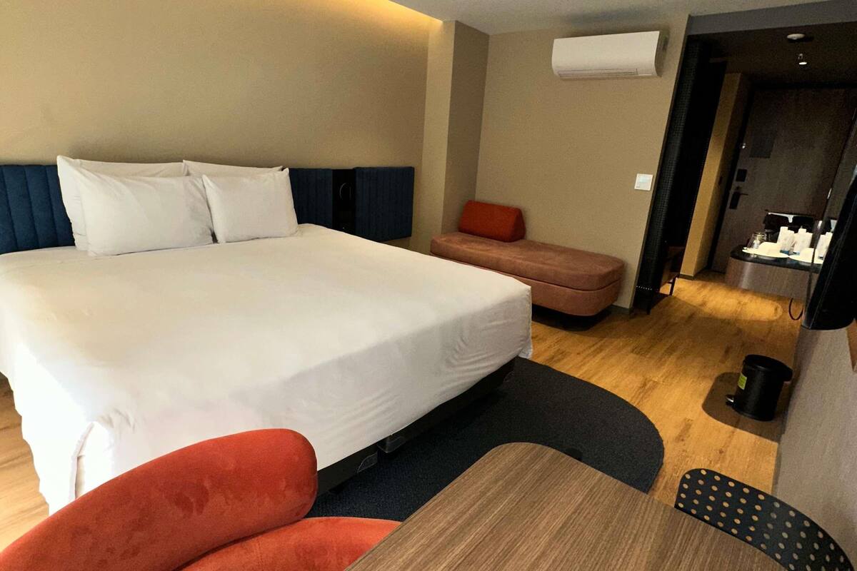 Una habitación de hotel con una cama grande, una zona de estar pequeña, una mesa de madera y una kitchenette.