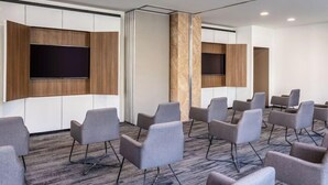 A conference room with grey upholstered chairs, a large flat-screen TV mounted on a wooden panel, and a carpeted floor. - Novotel México City Centro Histórico (Mexico City)