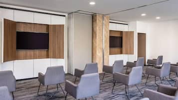 Un salón de conferencias con sillas tapizadas en gris, un televisor de pantalla plana grande montado en un panel de madera y suelo alfombrado.