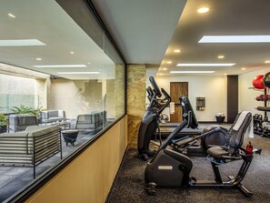A modern gym with exercise equipment, a seating area with chairs and a table, and a view through a glass wall. - Novotel México City Centro Histórico (Mexico City)