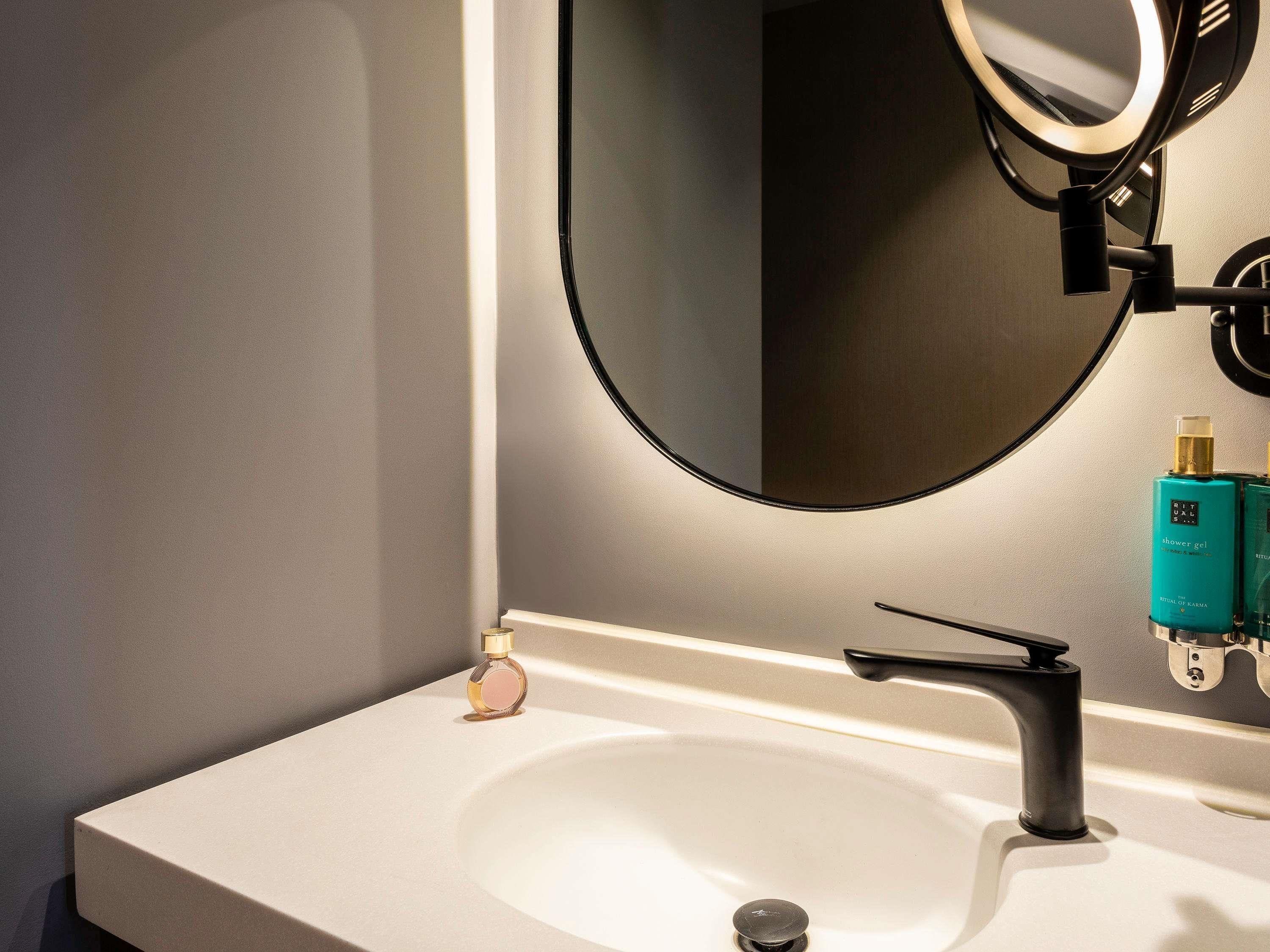 A bathroom with a white sink, a black faucet, a mirror, and a bottle of Rituals shower gel.