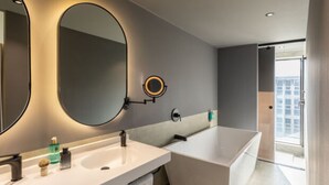 A modern bathroom with a large mirror, two sinks, a bathtub, and a view of a cityscape. - Novotel México City Centro Histórico (Mexico City)