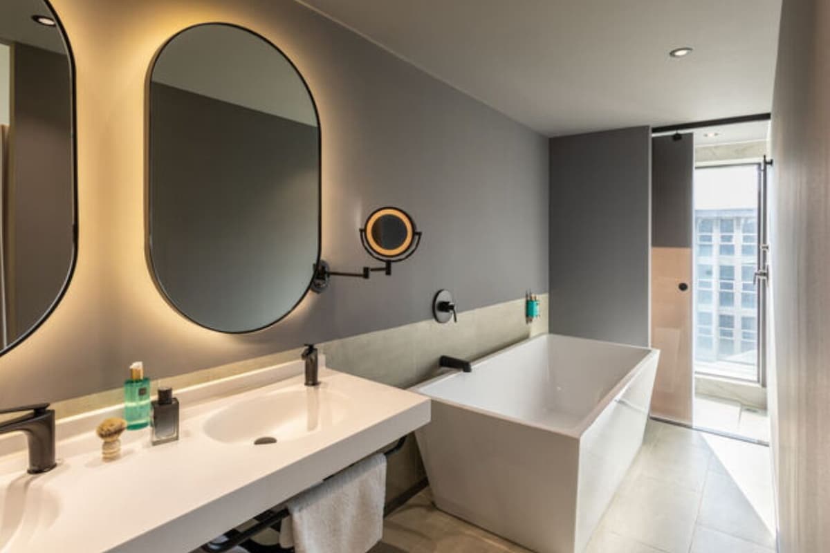 A modern bathroom with a large mirror, two sinks, a bathtub, and a view of a cityscape.