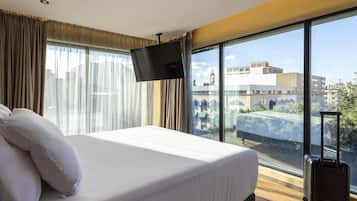 Ein Hotelzimmer mit einem großen Bett, einem Flachbildfernseher und Blick auf die Stadt durch raumhohe Fenster.