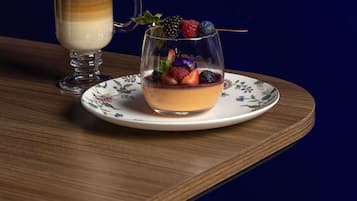A dessert in a glass bowl on a floral plate, with a layered beverage in a glass mug beside it.