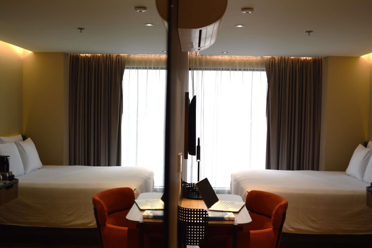 A hotel room with two beds, a desk with a laptop, and a chair.