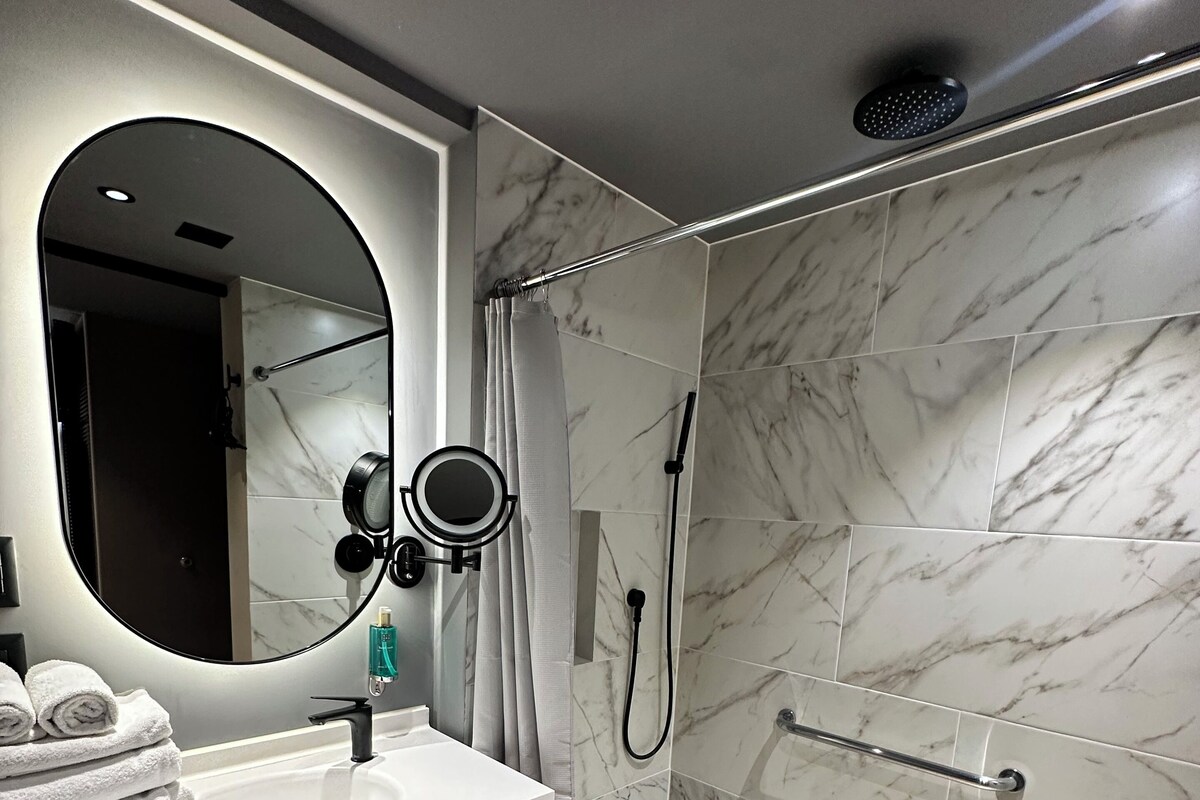 A modern bathroom with a marble shower, a vanity with a mirror, and a sink.