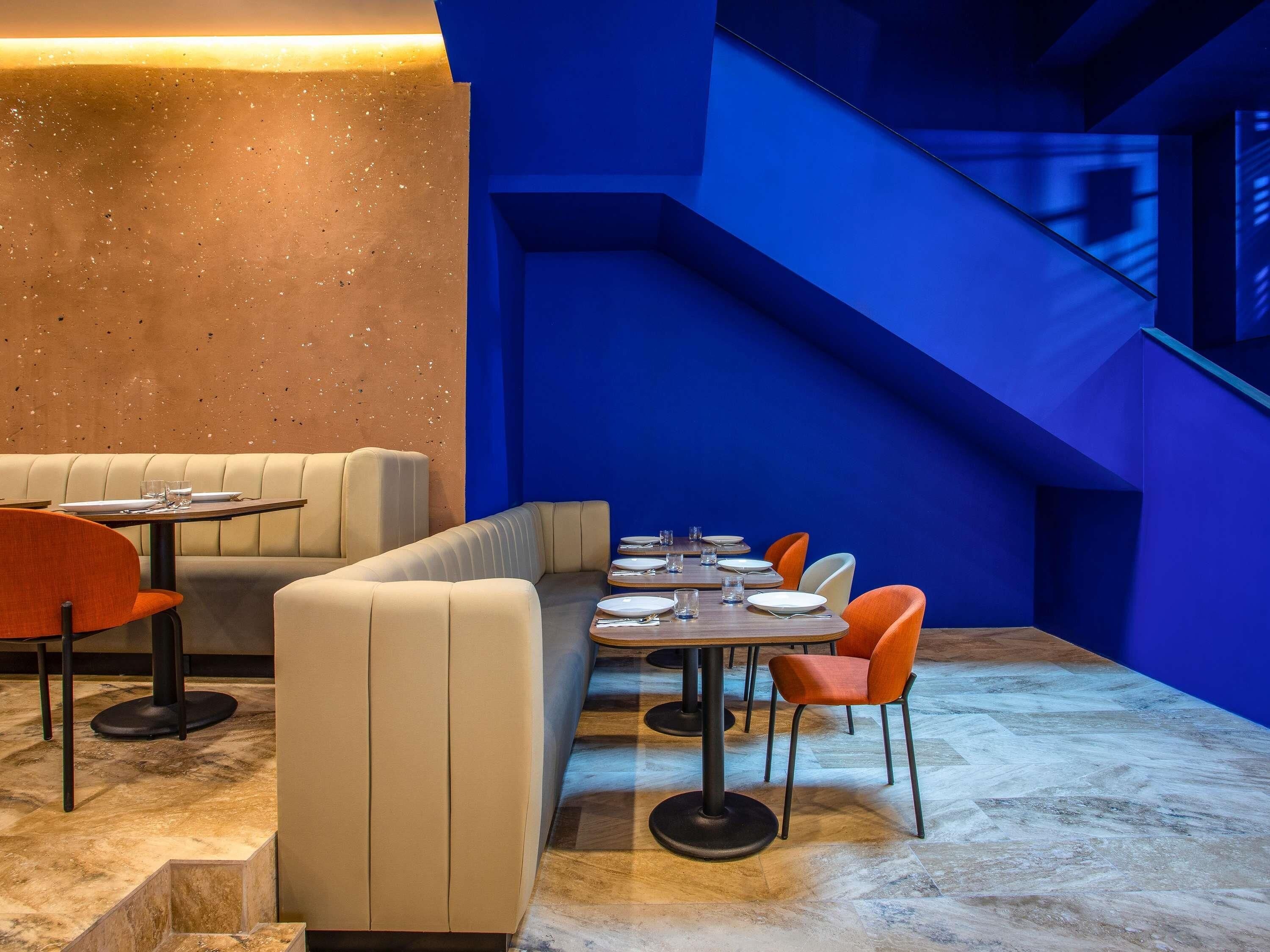 Een restaurant interieur met een zithoek met afgesloten ruimtes, een lange tafel met stoelen, en een blauwe accentmuur.