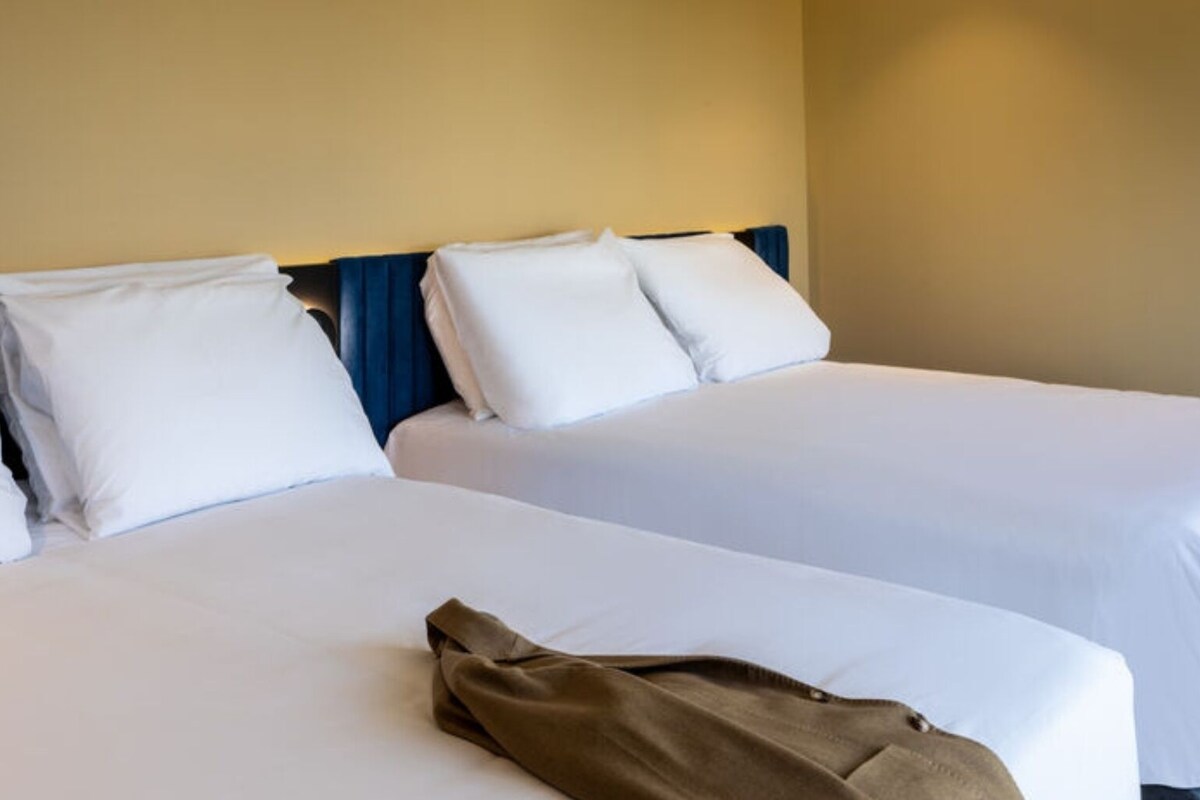 Two single beds with white linens, a blue headboard, and a brown jacket on the floor.