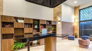 A modern lobby with a central black table, wooden bookshelves, a potted plant, and a seating area with a blue sofa and a pink ottoman. - Novotel México City Centro Histórico (Mexico City)