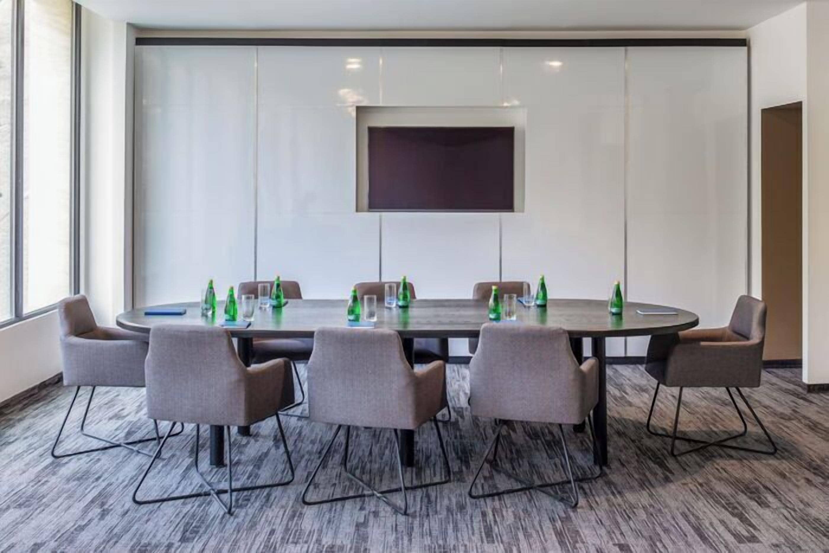A conference room with a large table, six chairs, and a large screen on the wall.
