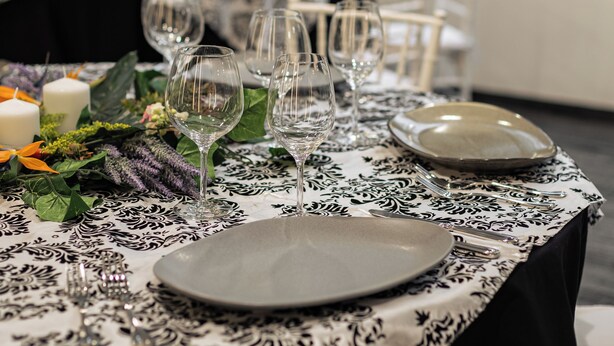Una mesa de comedor dispuesta con platos, vasos y velas, rodeada de sillas.