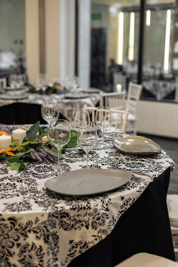 A dining table set with plates, glasses, and candles, surrounded by chairs.