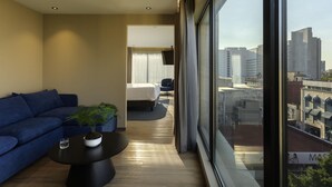 Ein modernes Hotelzimmer mit großem Fenster, einer Couch, einem Couchtisch und einem Bett.