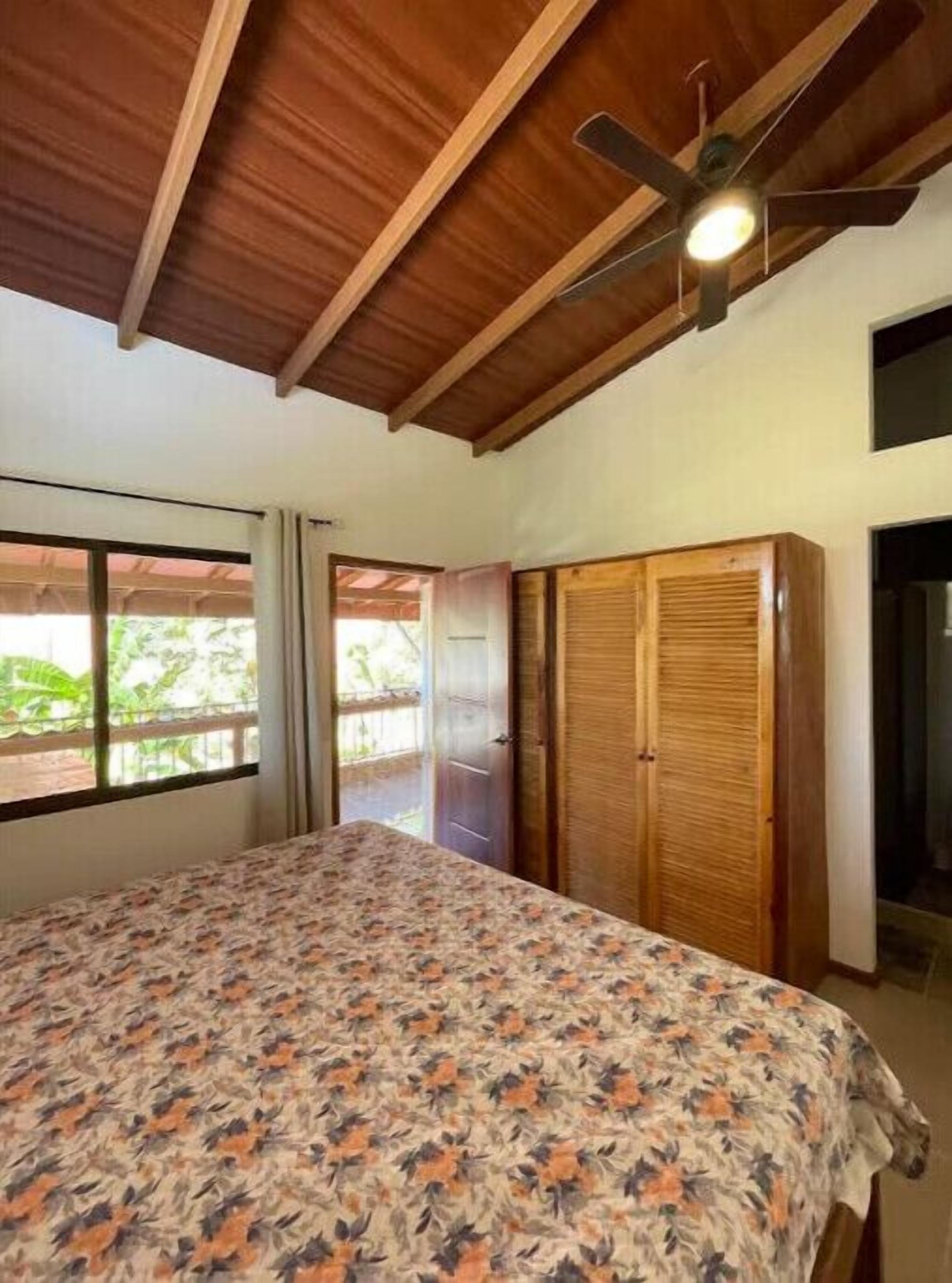 A bedroom with a bed, a ceiling fan, and a window with curtains.