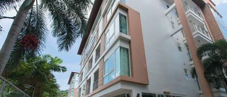 A modern building with a glass facade, a pool area, and a well-maintained garden with palm trees.