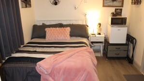 Un dormitorio con cama, mesita de noche, cómoda, microondas y ventilador.