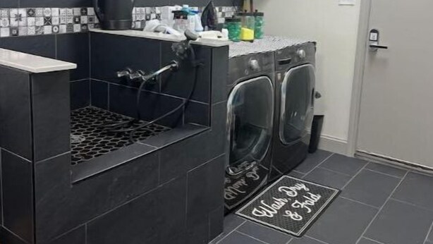 Een praktische wasruimte met een wasmachine, droger en een spoelbak. Er hangen decoratieve wanddecoraties en is een klein aanrecht met diverse spullen.
