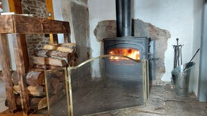 A stone fireplace with a black chimney, a metal screen door, and a stack of firewood.