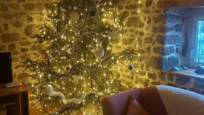 A cozy living room with a stone wall, a wooden ceiling, and a Christmas tree adorned with lights.
