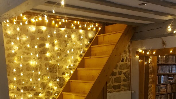 A staircase with wooden steps and a stone wall, illuminated by string lights.