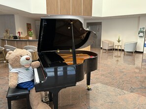 A grand piano in a spacious lobby with a plush teddy bear seated on it. - Brit Hotel Privilège Paris - Rosny (Rosny-sous-Bois)