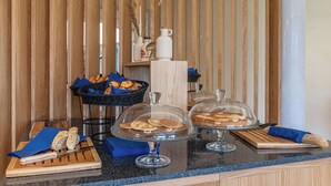 A breakfast buffet with bread, pastries, and a cutting board with a knife. - Brit Hotel Privilège Paris - Rosny (Rosny-sous-Bois)