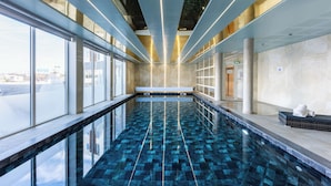 An indoor swimming pool with a clear view of the outside through large windows, a bench along the pool, and a tiled floor. - Brit Hotel Privilège Paris - Rosny (Rosny-sous-Bois)